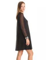 Vestido negro de seda fría con silueta evasé, cuello redondo y mangas largas de gasa transparente. Los puños son anchos y están decorados con una densa aplicación de perlas blancas.