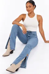 Jeans de tiro alto con lavado claro y diseño acampanado. Presenta aberturas laterales en los bajos con detalles de parches de cuero en los extremos y dobladillos deshilachados.