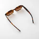 Lentes de sol con armazón ovalado de policarbonato gris traslúcido y cristales oscuros, con filtro UV400 y diseño versátil.