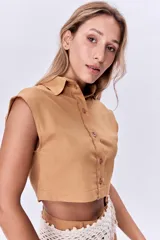 Camisa corta color ocre de lino, con cuello clásico, cierre frontal con botones y mangas cortas con solapas.