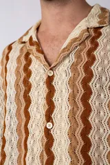 Camisa de manga corta confeccionada en tejido de crochet con diseño de ondas verticales en tonos tierra y beige. Presenta cuello solapa y cierre frontal con botones.