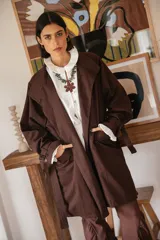 Trench de gabardina color chocolate con silueta relajada, cierre frontal con botones, bolsillos amplios y lazos regulables en los puños. Presenta un diseño con solapa en la espalda y lazo desmontable en la cintura.