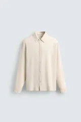 Camisa de hombre de corte relajado (relaxed fit) en tejido de mezcla de algodón y viscosa, color beige claro con finas rayas verticales. Presenta cuello italiano y manga larga con puño abotonado.