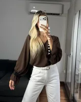 Blusa de tela cey color bordó, con escote en V y mangas largas abullonadas que terminan en puños con detalle de encaje y volados.