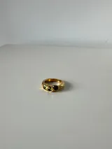 Anillo de acero quirúrgico con acabado dorado y tres piedras circulares de color verde engarzadas en la parte superior.