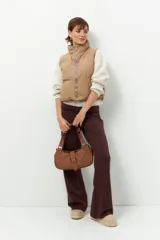 Chaleco puffer color beige, sin mangas, con cuello alto y cierre frontal con cremallera.