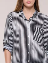 Camisa de corte clásico y silueta relajada con diseño de rayas verticales en blanco y negro. Presenta cuello camisero tradicional, cartera frontal con botones, un bolsillo aplicado en el pecho con rayas horizontales y mangas largas con sistema para arremangar.