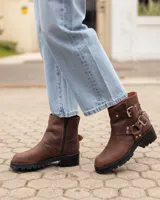 Botas cortas de cuero color caoba, con suela track negra, cierre lateral y correas con hebillas metálicas decorativas.