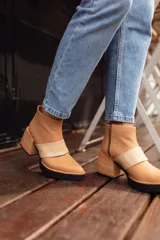Botinetas de cuero color tostado con diseño de punta fina y taco cuadrado de madera. Presentan una banda horizontal de charol en tono más claro sobre el empeine y suela de goma negra.