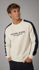 Buzo de cuello redondo color crema con franjas laterales en color azul marino en las mangas. Presenta estampado frontal con el logo de la marca Duxon Jeans y detalles en tipografía.