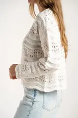 Sweater de punto calado con diseño de ondas horizontales, cuello redondo y mangas largas. Presenta un corte oversize y acabado en color blanco.
