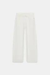 Jeans de mezclilla azul claro, tiro bajo, con corte ancho y pierna recta. Presenta un detalle de cintura cruzada o vuelta con un nudo o pliegue frontal y un ligero desgaste en una de las piernas.