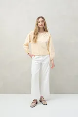 Blusa color verde claro de algodón con cuello a la base y bordados calados en el canesú. Presenta mangas largas con pequeñas aberturas lineales y ajuste con elástico en el puño.