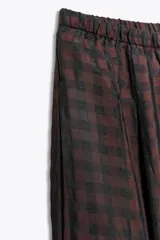 Pantalón de tiro medio con cintura elástica ajustable y cordón de ajuste. Diseño holgado con patrón de cuadros pequeños en tonos marrón oscuro y negro. Los bajos terminan en puño elástico.