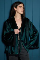 Kimono de terciopelo color verde oscuro, con mangas largas acampanadas y cierre frontal mediante tiras para anudar. Presenta detalles de puntilla negra en los bordes del cuello, mangas y ruedo.