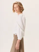 Camisa blanca de diseño femenino con volados en las mangas. Presenta una combinación de texturas, con algodón de camisa en el frente y mangas, y algodón con spandex en la espalda para mayor comodidad. Posee mangas largas con puños elásticos.
