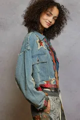 Campera de jean con textura acanalada, cierre frontal y diseño con apliques de estrellas desgastadas. Presenta detalles de tela escocesa en los puños y el ruedo, con bordes desflecados y bolsillos frontales con solapa.
