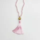 Japa mala compuesto por 108 cuentas de cuarzo rosa, con un dije central de madera y una borla de hilo de seda en color rosado.
