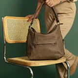 Cartera tipo hobo de cuero sintético color rojo ladrillo, con correa de hombro ajustable. Tiene cierre superior con solapa y broche magnético, bolsillo frontal con cierre, bolsillos laterales con cierre y múltiples bolsillos internos.