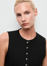 Chaleco de corte recto y diseño sin mangas, con cuello redondo y cierre frontal mediante botones con efecto joya. Presenta dos bolsillos de ribete laterales y forro interior.