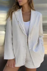 Blazer de lino natural color beige, con solapa clásica decorada con un delicado volado, cierre frontal de dos botones y bolsillos frontales aplicados.
