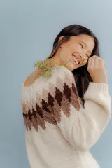 Buzo tejido a mano en lana merino, con diseño de patrón geométrico en forma de rombos en la parte superior en tonos marrones sobre base color crema.
