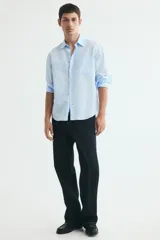 Camisa en mezcla de lino y algodón color celeste, de corte relajado, manga larga, con cuello inglés, bolsillo frontal y cierre de botones.