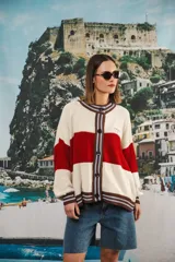 Cardigan oversized de punto grueso, color azul marino y blanco con franjas rojas y rosadas en el cuello, puños y solapa. Tiene botones grandes marrones y el logo de Anthea bordado en el pecho.