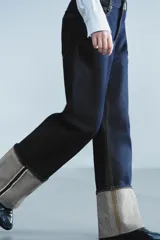 Jeans de tiro bajo y pernera ancha, confeccionados en denim azul oscuro con pespuntes en contraste. Cuentan con un diseño de cinco bolsillos, cierre frontal con cremallera y botón metálico, y destacan por su amplio doblando en el bajo que deja ver el revés de la tela con detalles de costura selvedge.