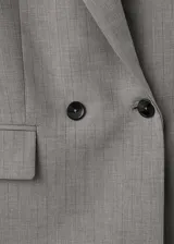 Blazer de corte recto y diseño estructurado, confeccionado en tejido mezcla de lana. Presenta cuello con solapas de muesca, cierre frontal de doble botonadura, bolsillos laterales con solapa y bolsillo de ribete en el pecho. Incluye forro interior y mangas largas con puños abotonados.