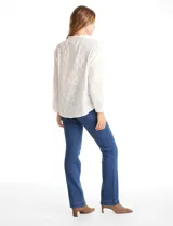 Blusa de algodón con diseño de broderie floral, cuello a la base, cierre frontal con botones y mangas largas amplias.