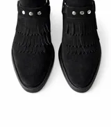 Botinetas de gamuza negra con flecos decorativos en el empeine y detalle de tachas metálicas. Incluyen una correa con estribo desmontable.