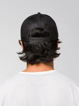 Gorro trucker negro de cinco paneles con malla en la parte trasera, visera curva y parche frontal redondo con el logo de Cat en amarillo.