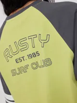 Remera bicolor Rusty de corte holgado y estilo deportivo, con cuerpo blanco y mangas raglán azules con doble raya blanca. Presenta estampado frontal con el texto 'RUSTY 85'.