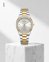 Reloj analógico de pulsera con movimiento de cuarzo japonés, caja de metal y malla de eslabones combinada en tonos plateado y dorado. Presenta un bisel decorado con cristales y esfera minimalista con índices.