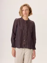 Camisa de lino rústico color marrón oscuro, con cuello mao, botones frontales y detalles de volados en el frente. Mangas largas con puños fruncidos.