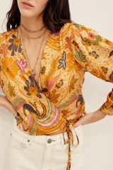 Camisa tipo cruzada (wrap) de manga larga con estampado floral multicolor en tonos mostaza y bordó. Cuenta con escote en V cruzado y detalle de lazo lateral con flor aplicada.