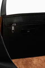 Bolso tipo shopper de color negro, con textura lisa y asas de mano. Cuenta con un compartimento interior con cierre y forro.