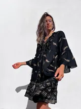 Túnica corta negra con estampado dorado de hojas y motivos geométricos, escote en V y mangas acampanadas.