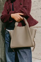 Bolso bandolera de formato city en color gris topo, con pespuntes decorativos, doble asa de mano, cremalleras laterales y cierre imantado.