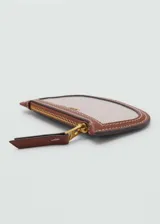 Monedero ovalado de tejido canvas color beige con ribete de cuero marrón. Tiene cierre de cremallera y logo en relieve.