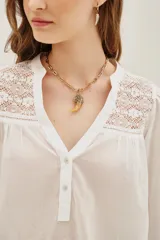 Camisa de algodón color celeste, con cuello mao, cierre frontal parcial con botones y detalles de encaje en los hombros y canesú. Presenta mangas largas abullonadas con puños elásticos.