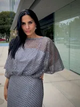 Vestido largo de fiesta color gris, confeccionado en tejido con textura calada tipo red. Presenta un diseño de silueta fluida con mangas amplias tipo murciélago y escote redondo.