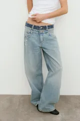 Jeans de tiro medio con cinco bolsillos, cintura doble a contraste y detalles de rotos. Cierre frontal con cremallera y botones metálicos.