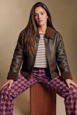 Campera tipo gamulán de cuero sintético en color marrón, con interior y detalles en cuello y puños de corderito sintético al tono. Presenta un corte oversize con cierre frontal metálico.