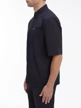 Camisa negra de manga corta con corte boxy, cuello en punta, bolsillo de parche en el pecho y logo CK bordado.