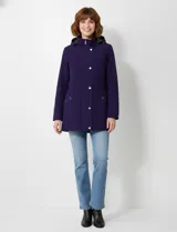 Gabardina impermeable de mujer, color morado oscuro, con capucha desmontable y cierre frontal oculto con botones a presión. Presenta bolsillos delanteros y ajuste interno en la cintura.