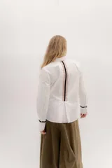 Camisa de manga larga color celeste claro, con cuello camisero y botones frontales. Presenta un detalle de cinta negra alrededor del puño doblado.