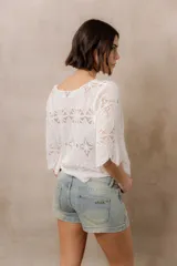 Blusa de punto calado color blanco, con diseño geométrico y floral transparente, escote redondo y mangas tres cuartos amplias de calce relajado.