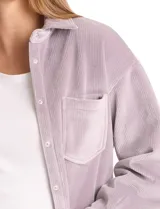 Sobrecamisa de pana con textura acanalada, corte oversize y silueta holgada. Presenta cuello clásico, cierre frontal con botones metálicos, mangas largas con puños abotonados y dos bolsillos frontales tipo parche con solapa.